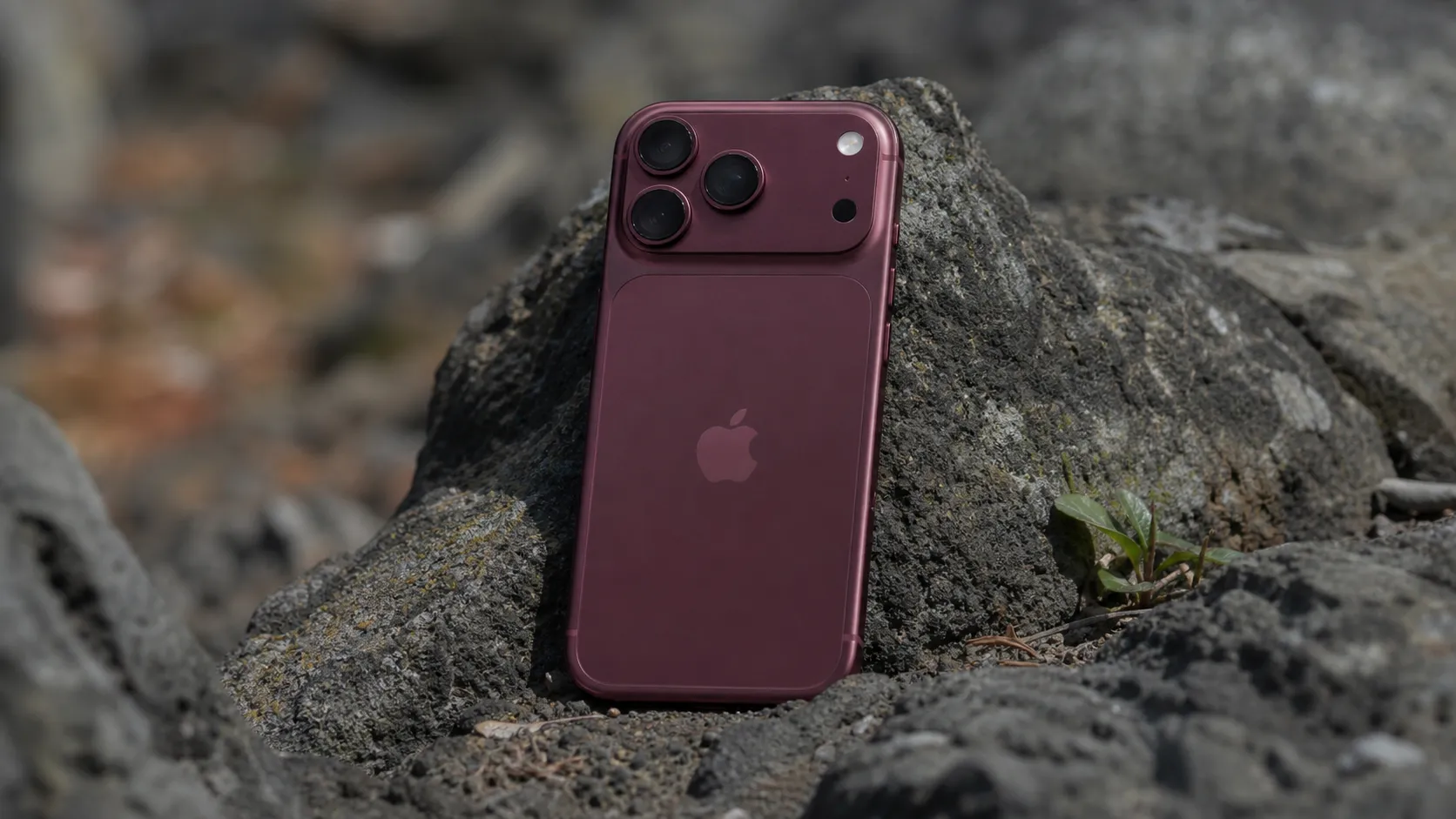 Burgundy iPhone 18 Pro resting on dark outdoor rocks displaying the mechanical camera system.